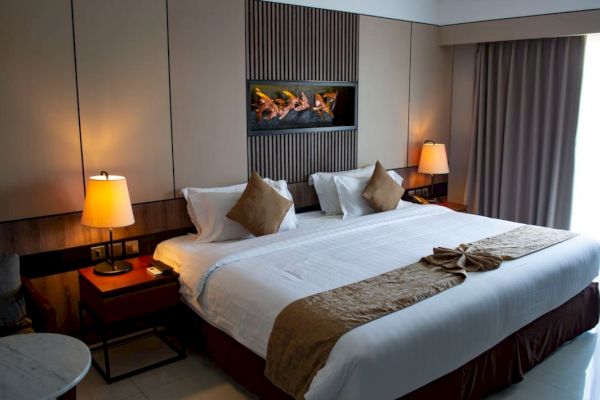 The image shows a cozy hotel room with a large bed, two bedside tables with lamps, and a window with curtains drawn.
