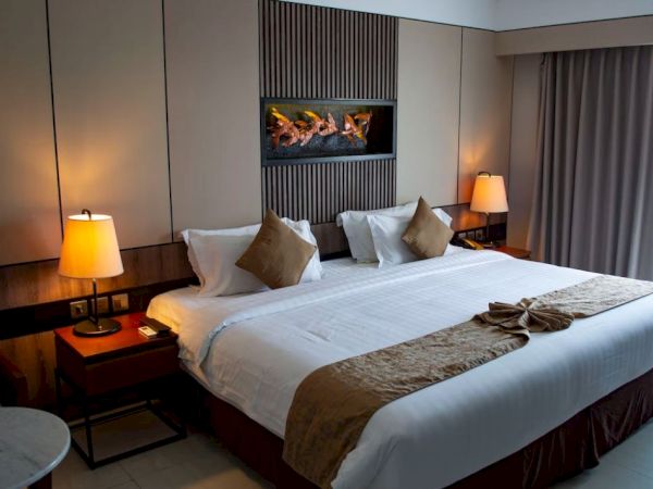 The image shows a cozy hotel room with a large bed, two bedside tables with lamps, and a window with curtains drawn.