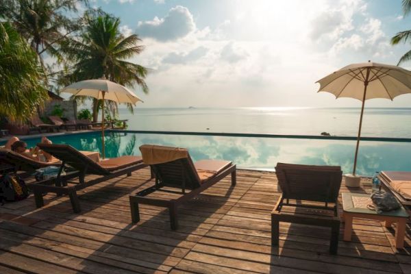 A stunning beachfront scene with lounge chairs, umbrellas, and a serene pool overlooking the ocean under a partly cloudy sky, creating a tranquil atmosphere.