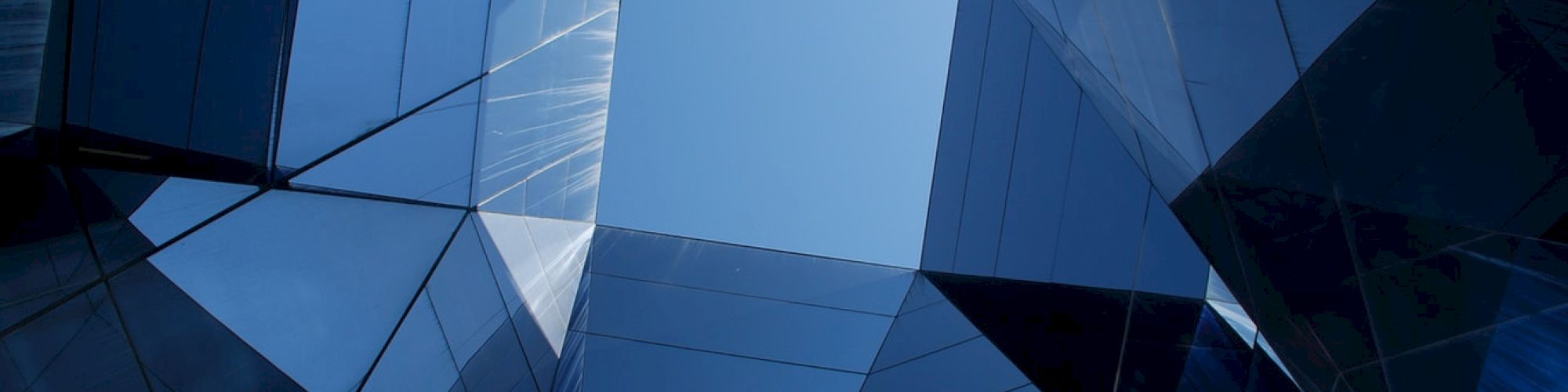 The image shows a perspective view of a geometric structure made of reflective glass panels forming a pattern with the sky visible in the center.