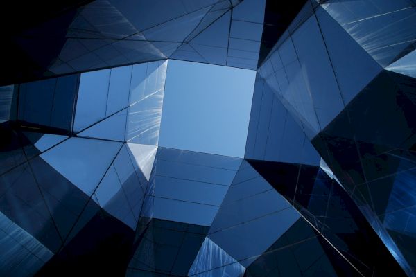 The image shows an architectural design featuring glass panels, creating geometric patterns with a central open space through which the sky is visible.