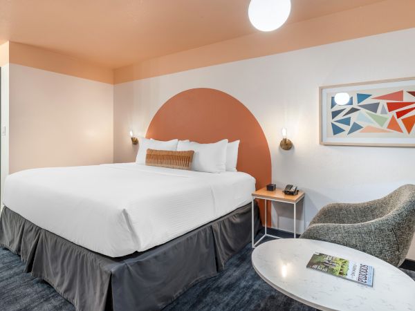 A modern hotel room with a large bed, abstract art, a small table, and a chair.