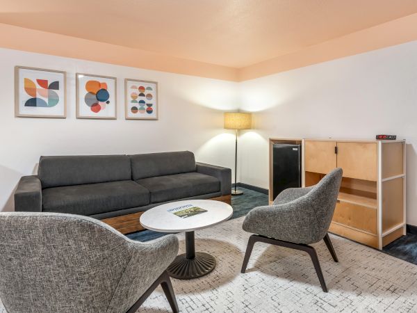 A modern living room with a gray sofa, two chairs, a round table, and a lamp, featuring abstract art on the wall.