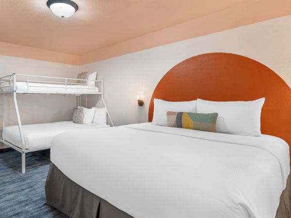 A hotel room with a large bed and a bunk bed, featuring modern decor and warm tones.