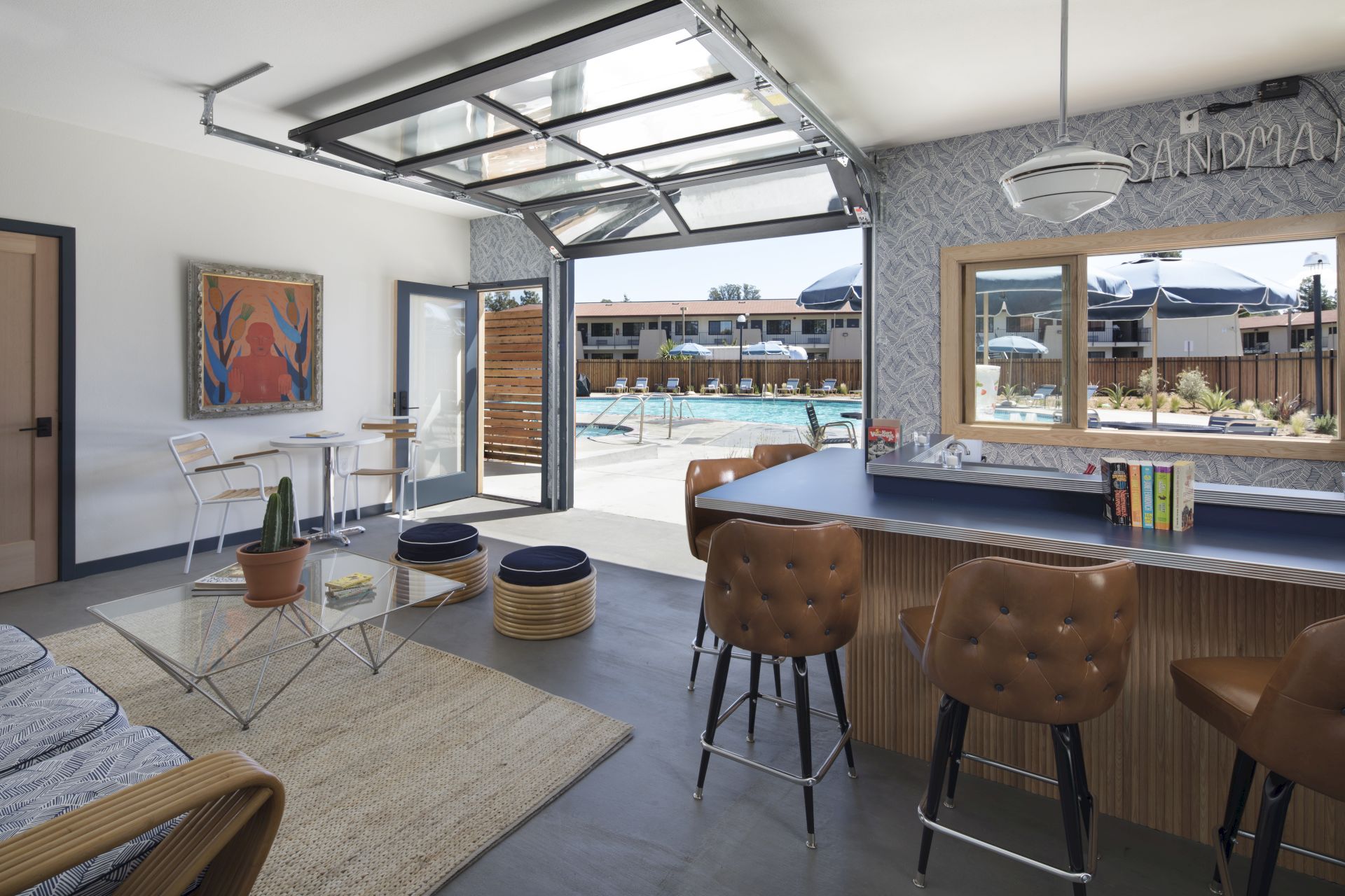 A modern indoor space with a bar and seating area opens up to an outdoor pool area, featuring stylish furniture and decor.