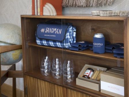 The image shows a wooden shelf with items including glassware, a picnic blanket, drink koozies, and snack kit. All items are labeled 