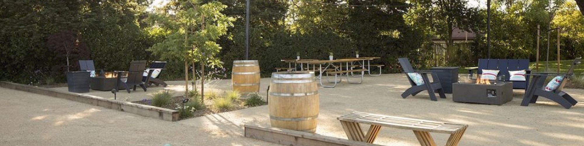 The image shows an outdoor space with seating and game setups, surrounded by tall trees. There are game balls scattered on the ground.