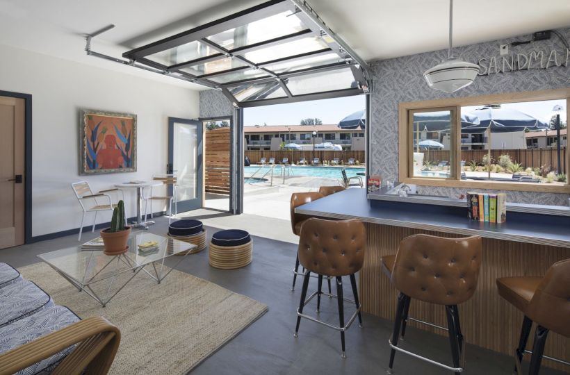 A modern, open space with a bar, lounge area, and large window overlooking an outdoor pool area, featuring stylish decor and seating.