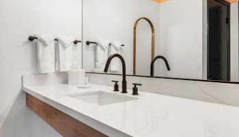 A modern bathroom with a white countertop, black faucet, large mirror, and towel rack holding white towels, under warm lighting.