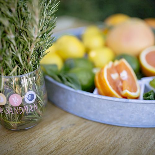 A close-up of fresh herbs in a glass jar next to a tray of various citrus fruits, including lemons, limes, and grapefruits.