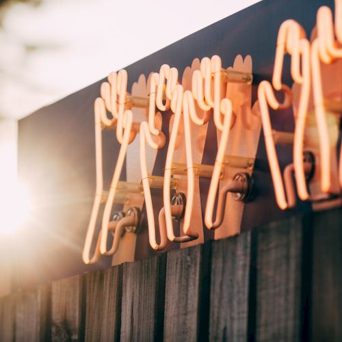 Neon lights in the shape of teeth on an outdoor sign, with a sun flare visible on the left side of the image.