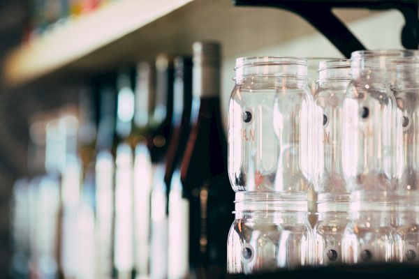 The image shows a row of glass jars stacked next to bottles on a shelf, possibly in a kitchen or bar setting.