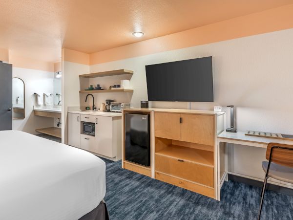 A hotel room with a bed, kitchenette, TV, desk, and bathroom area visible in the background.