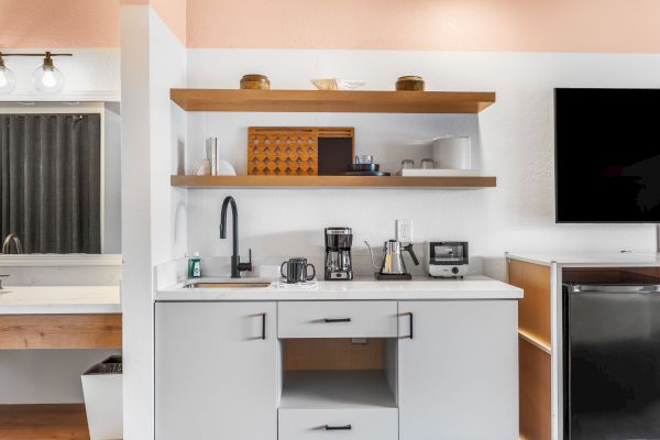 The image shows a modern kitchenette with open shelves, kitchen appliances, and a TV on the right side of the frame.