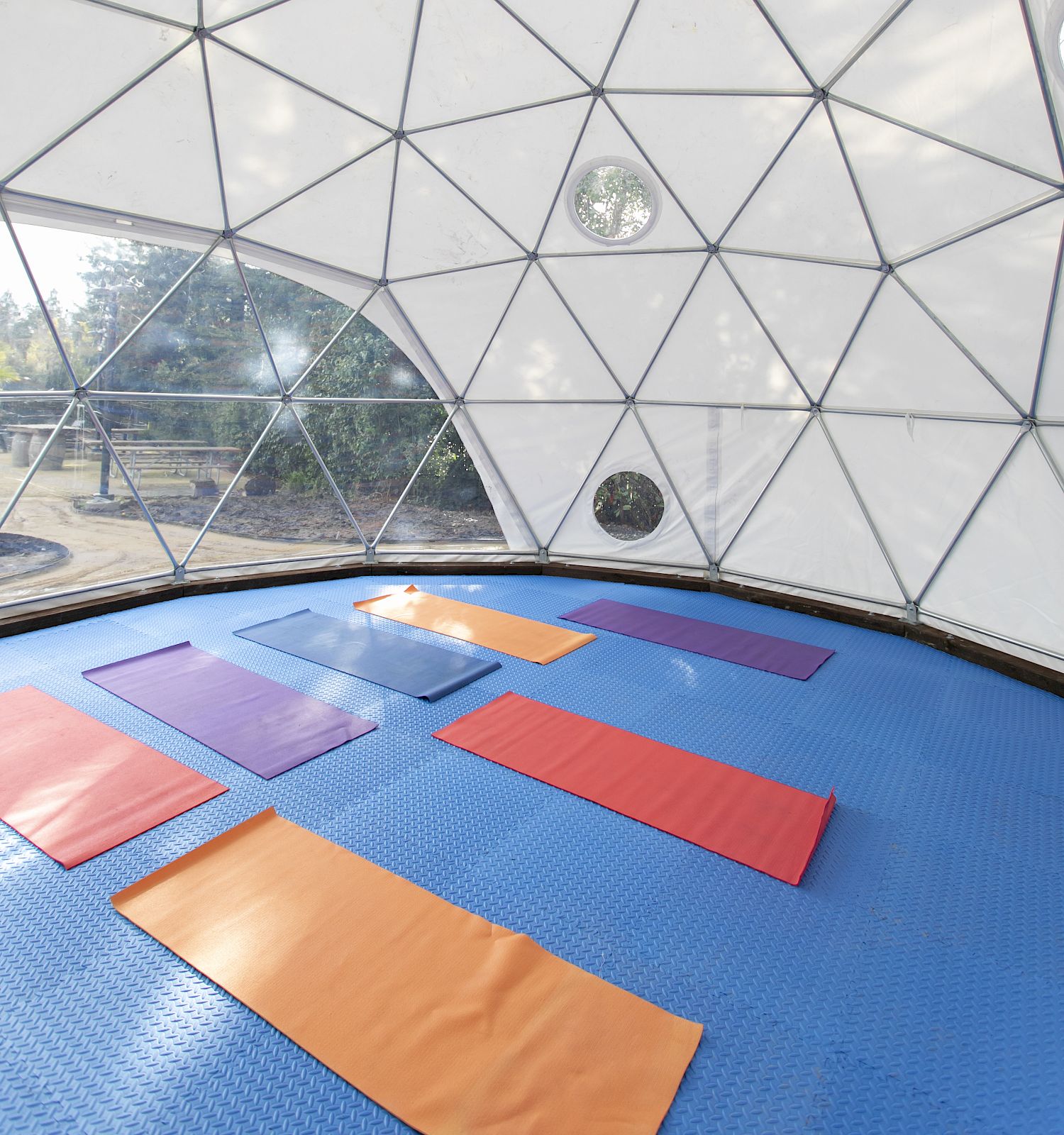 The image shows the interior of a geodesic dome with yoga mats placed on a blue floor, creating a serene and modern space for exercise or relaxation.