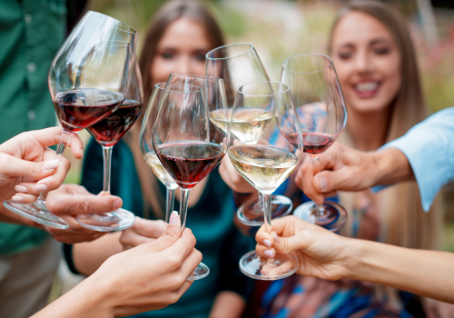 A group of people raising wine glasses in a celebratory toast, with both red and white wine visible.