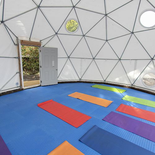 A dome-shaped room with a geometric design, colorful yoga mats on a blue floor, and an open door leading outside completes the scene.