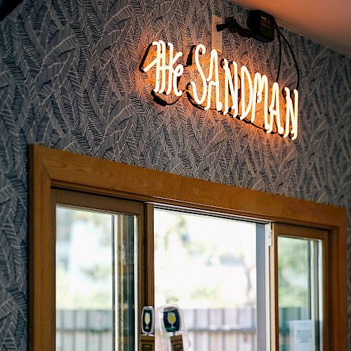 The image shows a bar area with a neon sign that reads "The Sandman" above a window, and two beer taps are visible in front of the window.