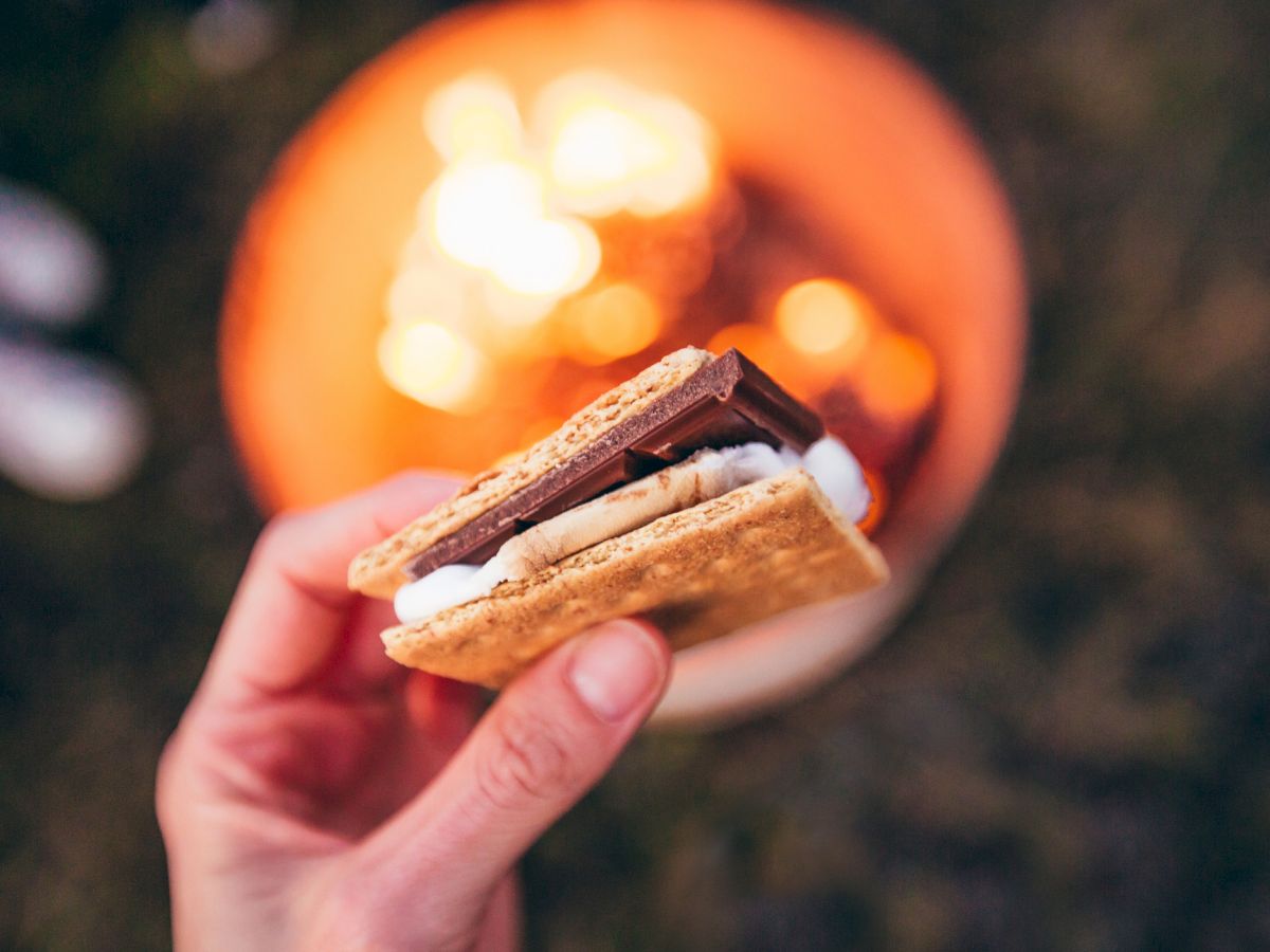 A hand holding a s'more in front of a warm, glowing campfire, capturing a classic outdoor treat.