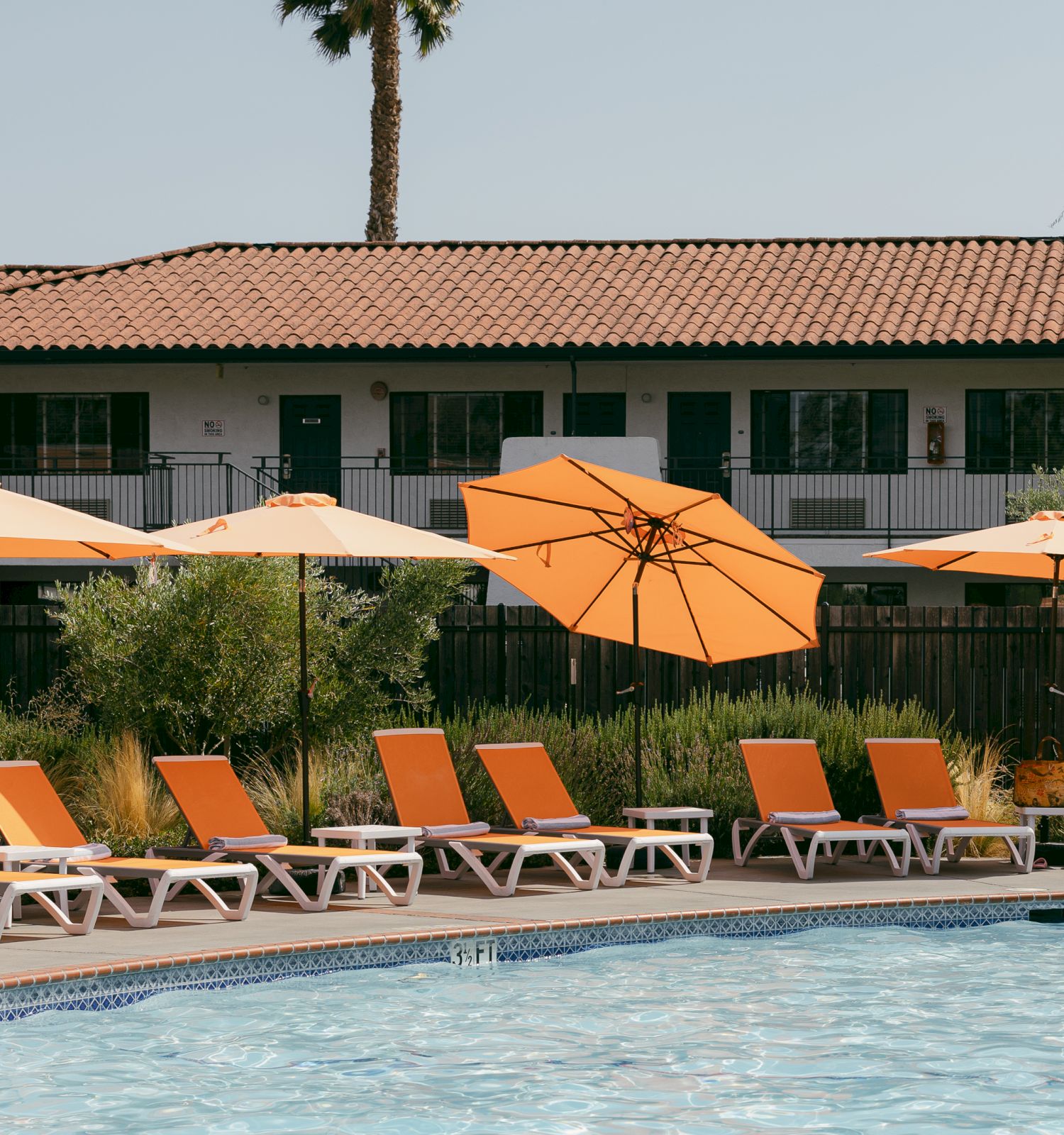 A poolside area with orange lounge chairs and umbrellas, with a building in the background, creating a relaxed atmosphere.