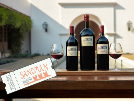 Three wine bottles and two glasses on a table outside, with a "SANDMAN" ticket on the side.