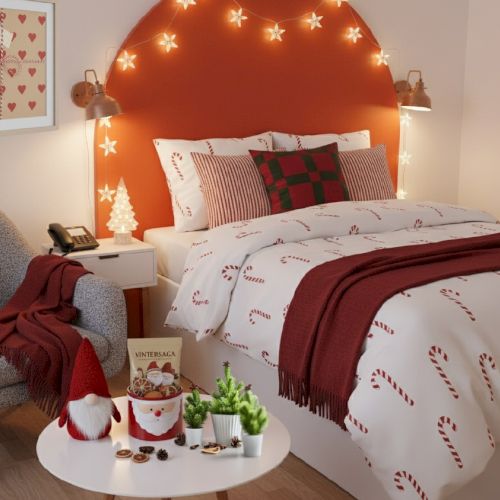 A cozy Christmas bedroom with a padded orange headboard, candy cane bedding, red accents, fairy lights, and a round coffee table with decorations, ending with a warm festive feel.