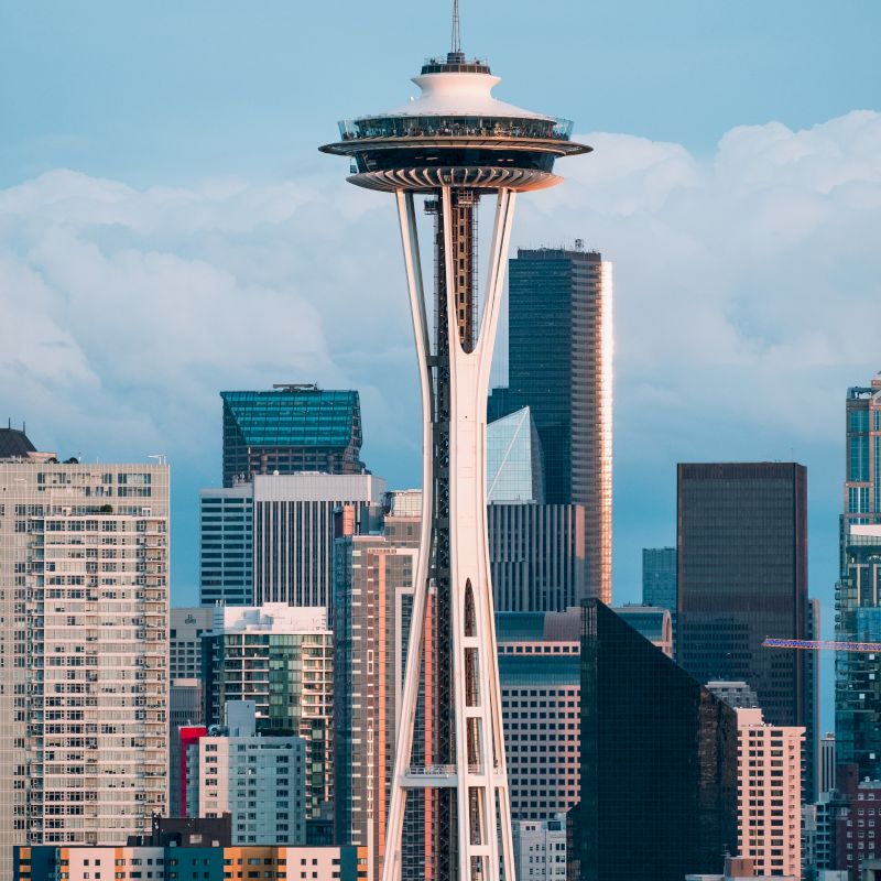 The image shows the Space Needle in Seattle with surrounding skyscrapers and a cloudy sky in the background.