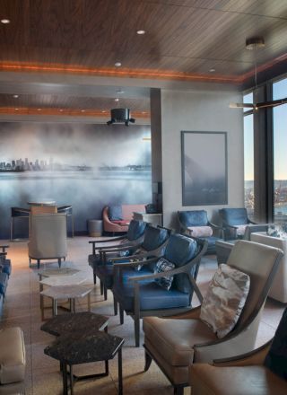 A modern lounge with multiple seating options, large windows offering a waterfront view, ambient lighting, and a mural on the back wall.