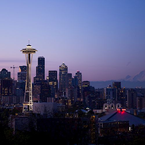 The image shows an evening view of Seattle's skyline with the iconic Space Needle in the foreground and Mount Rainier in the background.